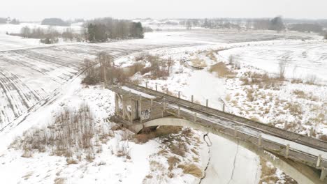 Aerial-view-of-abandoned-bridge-and-agricultural-field-during-winter-time