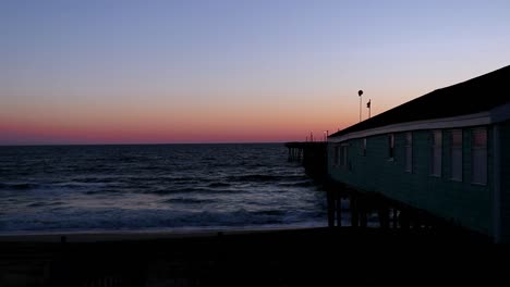 Clear-sky-at-sunrise-in-the-Outer-Banks-of-North-Carolina-as-waves-roll-onto-the-sand-beside-a-wooden-fishing-pier