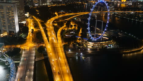 Singapur-Stadt---Circa-Zurückziehen-Nacht-Zeitraffer-Mit-Flieger-Riesenrad-Verkehr-Auf-Der-Autobahn-Türme-Gebäude-Stadtlichter-Und-Meer