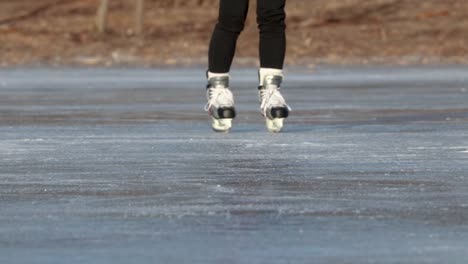 Close-up-shot-of-young-girl's-skates-on-frozen-lake-as-she-figure-skates