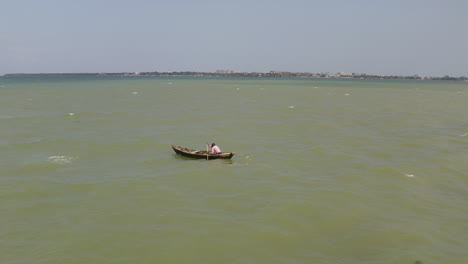 A-man-paddling-a-wooden-canoe-boat-against-the-wind-and-waves-on-a-sunny-day-near-the-coast-of-Dar-es-Salaam,-Tanzania