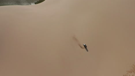 Aerial:-A-truck-with-kitesurfers-traveling-through-the-dunes-of-Lencois-Maranhenses-in-Brazil,-during-dry-season