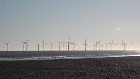 A-person-walks-on-beach-in-front-of-an-offshore-wind-turbine-farm-off-the-coast-of-Hartlepool-in-the-North-Sea