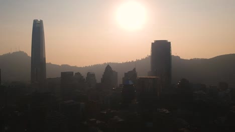 Aufsteigende-Luftaufnahme-Der-Skyline-Von-Santiago-Gegen-Die-Sonne