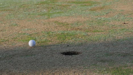 Putted-golf-ball-on-the-green-rolls-past-the-hole,-low-and-slow-motion
