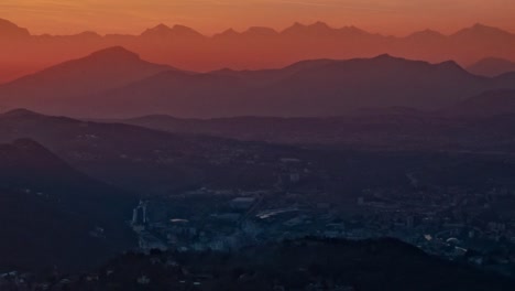 Stunning-sunset-color-caught-in-fog-and-haze-over-mountains-behind-town-in-valley-below