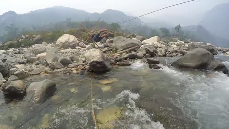 A-trainer-of-a-mountaineering-institute-of-the-Himalayas-crossing-the-mountainous-river-by-rope,-practicing-to-cross-the-river-with-rope