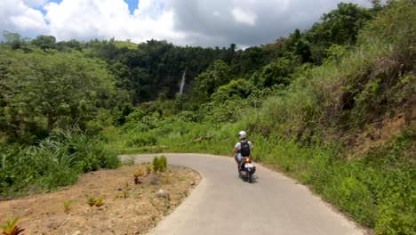 A-slow-following-shot-of-a-motorcycle-driving-down-a-Filipino-road-to-the-beautiful-Candijay-Waterfall-on-the-island-of-Bohol,-Philippines