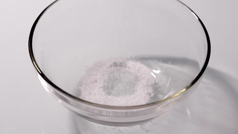 Slow-motion-shot-of-sugar-being-poured-into-a-glass-bowl-on-a-white-table