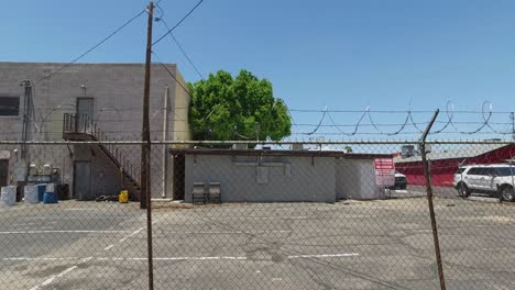 Muévete-Por-Un-Callejón-De-La-Ciudad-Más-Allá-De-Una-Valla-Encadenada-Coronada-Con-Alambre-De-Púas-Que-Encierra-La-Parte-Trasera-De-Un-Edificio-Industrial,-Sunnyslope,-Phoenix,-​arizona