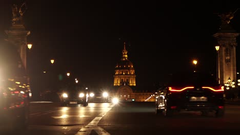 Traffic-driving-on-avenue-and-Les-Invalides-complex-on-background-at-night,-Paris