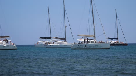 Wide-Shot-of-Four-Sail-Boats-Passing-By-Another-Sail-Boat-At-The-Ocean-Near-Santorini-Island-in-Greece