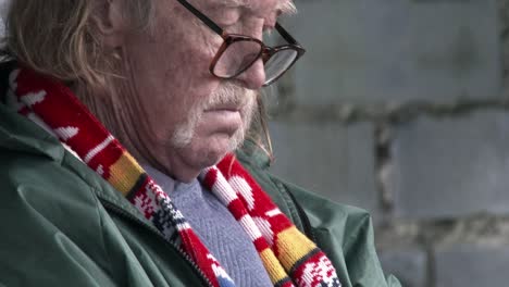 An-elderly-man-with-a-mustache,-dressed-warmly-reads-a-book-outdoors,-close-up