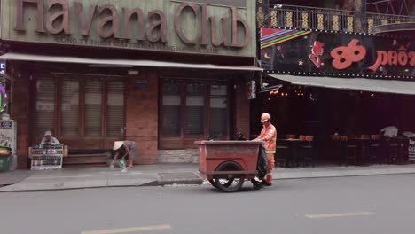 Garbage-collector-with-Cart-picking-up-rubbish-on-the-street-Bui-Vien-Steet,-red-light-district,-Ho-Chi-Minh-City,-Saigon,-Vietnam