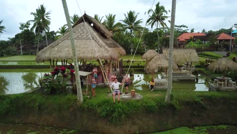 Drone-Shot-of-a-tourist-enjoying-a-swing-between-two-coconut-trees-that-swings-out-over-some-Rice-Terraces-in-Bali,-Indonesia