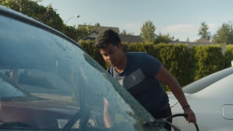 Teenage-boy-washing-the-door-of-a-vintage-car-on-a-driveway-in-the-evening