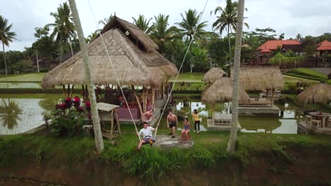 Drone-Shot-of-a-tourist-enjoying-a-swing-between-two-coconut-trees-that-swings-out-over-some-Rice-Terraces-in-Bali,-Indonesia