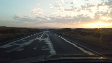 Slow-Motion:View-from-inside-car-on-empty-hilly-road-leading-to-horizon-line-at-sunset-or-sunrise
