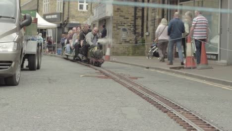 Adults-on-a-mini-steam-train-riding-backwards-in-town-center