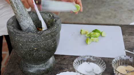 Close-up-shot,-female-chef-squeezing-fresh-green-lime-with-lime-drop-into-Stone-mortar