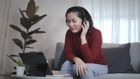 Businesswoman-redshirt-using-a-tablet-with-headphone-for-meeting-online-at-home