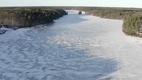 An-aerial-drone-shot-of-a-large-frozen-lake-with-a-group-of-people-ice-skating-on-the-surface---Daytime