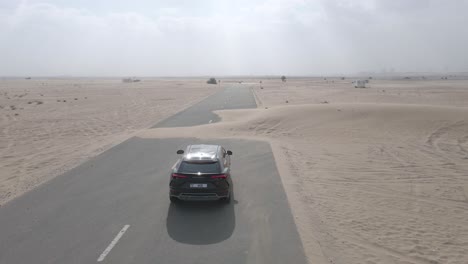 Black-Lamborghini-Urus-driving-amid-sand-dunes-on-desert-road-in-Dubai,-aerial