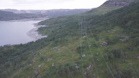 Aerial-View-of-power-lines-along-a-river-on-a-cloudy-day-in-Norway,-tracking-shot