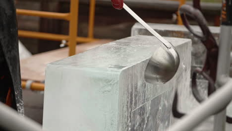 Sculptor-smoothing-ice-block-with-water-and-ladle,-Slow-Motion