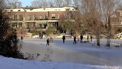 Sideways-moving-time-lapse-showing-people-in-winter-snow-landscape-enjoying-the-frozen-over-Great-Canal-in-Dutch-city-with-clouds-passing-by-in-blue-sky-ice-skating-and-fun-outdoor-leisure-scenes