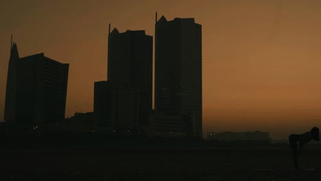 Silueta-De-Mujer-Haciendo-Yoga-En-La-Playa-De-Clifton-Contra-El-Cielo-Naranja-Del-Atardecer-En-Karachi