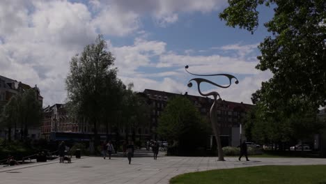 People-walking-by-the-Snake-statue-by-Phil-Price-in-Mølleparken,-Aarhus,-Denmark-on-a-hot-summers-day