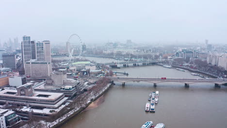 dolly-forward-aerial-shot-of-snow-falling-London-waterloo-bridge-south-bank-embankment-London-eye