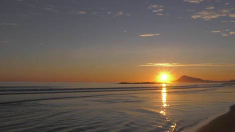 sunrise-over-calm-ocean-waves-washing-on-sandy-beach,-mediterranean-sea,-wide-angle,-spain