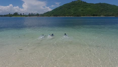 Three-kids-run-into-sea-at-Tanjung-Aan-Beach-on-Lombok-Island,-Indonesia