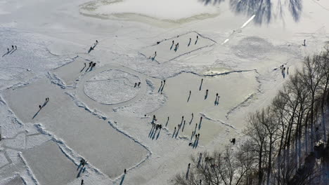 Aerial-view-of-people-on-ice-skating-on-frozen-lake,-skaters-having-fun-on-sunny-winter-day