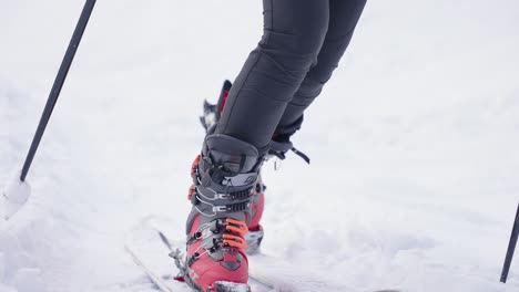 Close-up-on-woman-ski-boots-walking-through-snow-with-poles