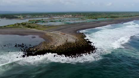 Oceanside-pier-and-coastal-salt-ponds-on-Glagah-Beach,-Java,-aerial-arc-shot