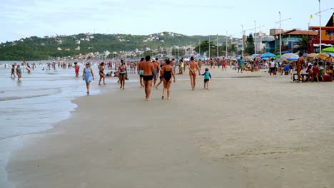 Dolly-in-of-tourists-walking-by-the-seashore-and-resting-in-the-sand-in-Bombas-and-Bombinhas-beaches,-Brazil