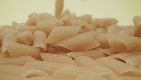 Real-time-probe-macro-footage-of-falling-mezze-penne-rigate-pasta-on-yellow-background
