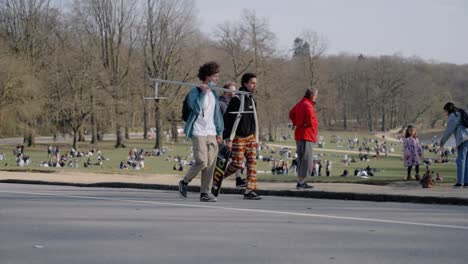 Young-hipsters-walking-with-skateboard-and-grind-rail-in-the-Bois-De-La-Cambre-in-Brussels,-Belgium---Slow-motion