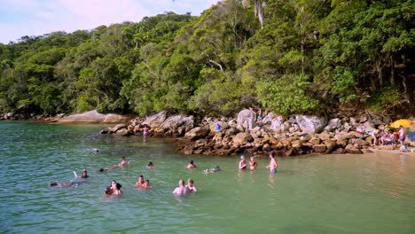 People-swimming-and-enjoying-summer-near-a-rocky-shore-and-woods-in-Praia-da-Sepultura,-Brazil