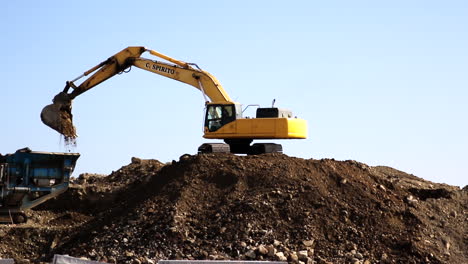 Digger-dumping-soil-into-a-truck,-vehicle-positioned-on-mound-of-earth