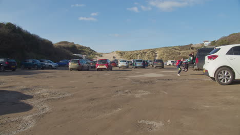 People-on-parking-lot-at-popular-tourist-attraction-Crantock-Beach,-girls-hanging-out-waiting-by-the-car
