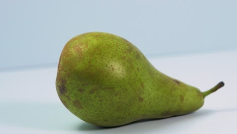 Fresh-big-green-pear-rotates-slowly-on-a-light-blue-background,-healthy-food-concept,-close-up-shot,-camera-rotate-left