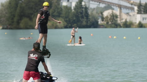 Slow-motion-track-shot-of-male-person-with-helmet-during-flyboard-exercise-with-trainer-on-jet-ski