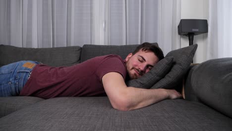 Happy-young-caucasian-man-takes-a-nap-on-a-sofa-in-a-modern-apartment