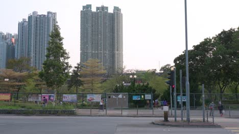 People-are-seen-gathering-and-walking-outdoors-near-a-park-as-the-sun-sets-in-while-traffic-goes-through-in-front-in-Hong-Kong