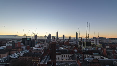 Wunderschöne-Weitwinkel-Sonnenuntergang-Zeitrafferansicht-Der-Skyline-Von-Manchester-Mit-Hohen-Gebäuden-Und-Riesigen-Baukränen,-Die-Sich-Bewegen-Und-Arbeiten,-Während-Wolken-Am-Horizont-Vorbeiziehen-Und-Die-Sonne-Untergeht