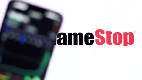 El-Precio-De-Las-Acciones-De-Gamestop-Se-Muestra-En-El-Teléfono-Inteligente-Contra-El-Logotipo-De-Gamestop-En-El-Fondo-Con-Rackfocus